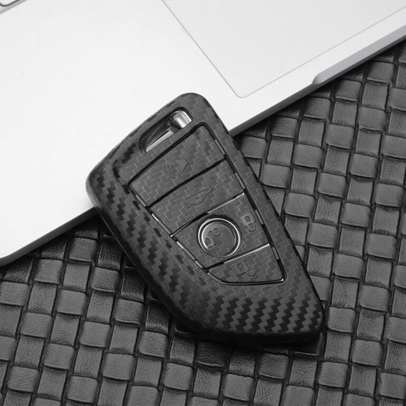 Replacement 4-button smart key case for BMW – carbon fibre case alone on a woven leather surface