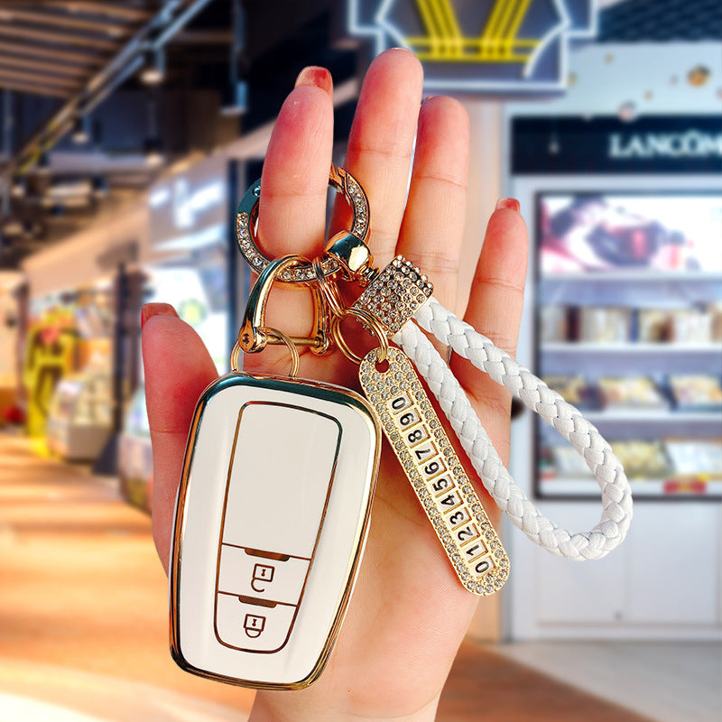 Key fob cover for Toyota 2-button keys – TPU – white and gold cover held in hand with crystal keyring and white braided wrist strap